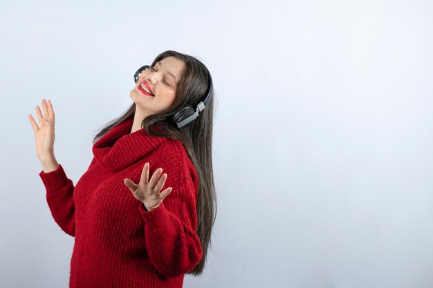 Une jeune femme souriante en pull chaud rouge écoutant de la musique dans les écouteurs