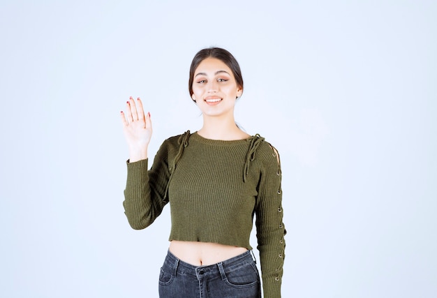 Une jeune femme souriante en pull vert agitant la main.