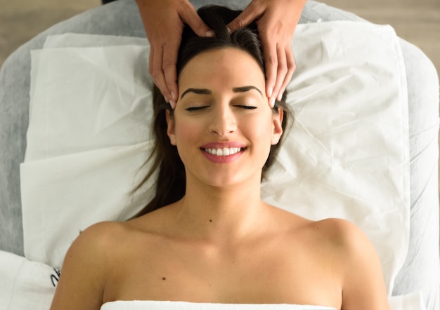 Jeune femme souriante recevant un massage de la tête dans un centre de spa.