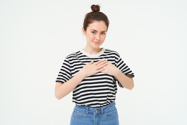 Photo gratuite la jeune femme souriante ressent la gratitude reconnaissante pour quelque chose tient les mains sur le cœur et regarde tendrement