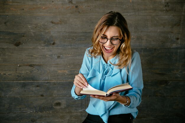 Jeune femme souriante en riant tout en lisant un livre. Vêtu d&#39;un chemisier élégant