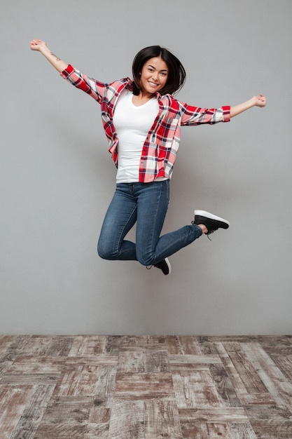 Jeune femme souriante sautant par-dessus le mur gris.