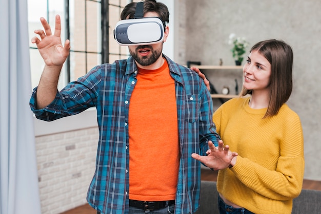 Photo gratuite jeune femme soutenant l'homme portant une caméra de réalité virtuelle touchant ses mains en l'air