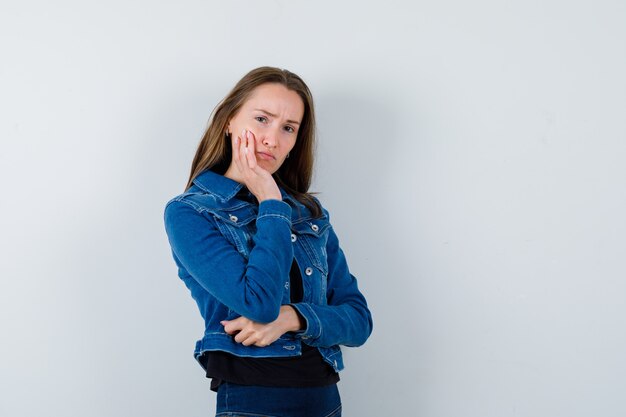 Jeune femme soutenant le menton sur la paume en chemisier, veste et regardant pensive.