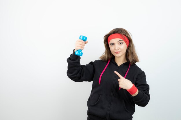 Jeune femme sportive debout et pointant vers l'haltère bleu. Photo de haute qualité