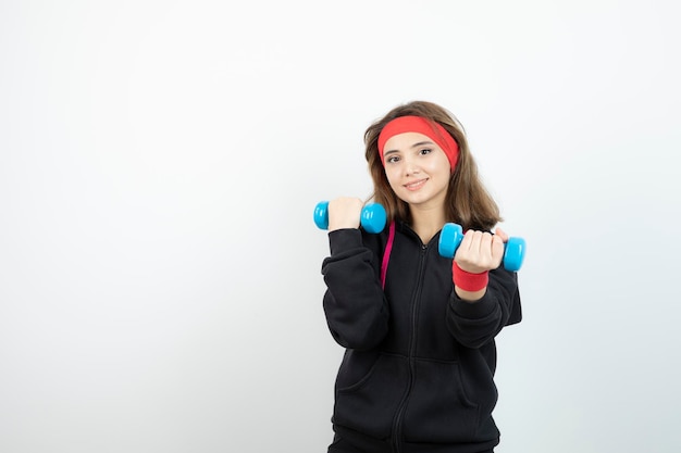 Jeune femme sportive debout et tenant des haltères bleus. Photo de haute qualité