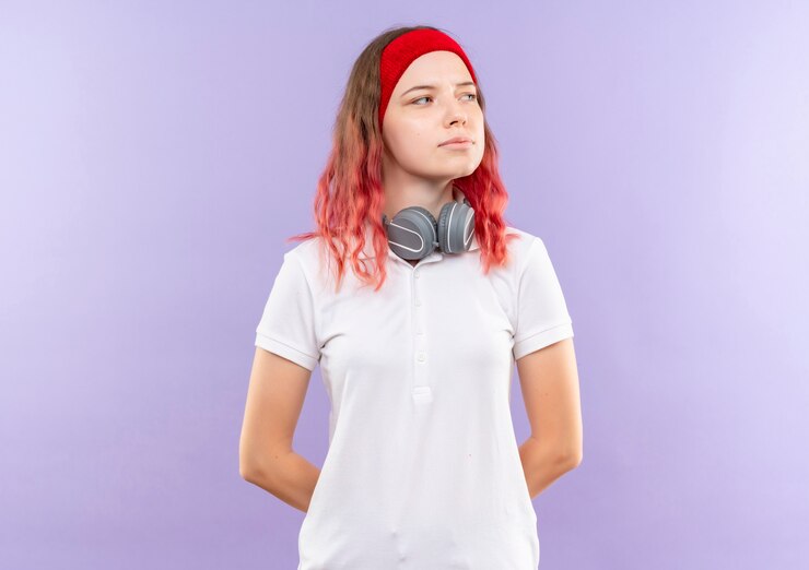 Photo gratuit jeune femme sportive avec des écouteurs à côté avec une expression confiante debout sur un mur violet