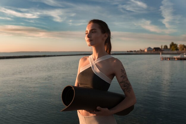 Jeune femme sportive à la plage debout avec tapis