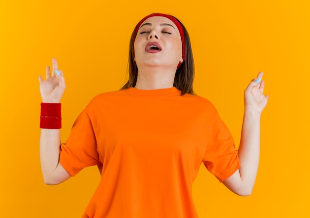 Jeune femme sportive portant un bandeau et des bracelets en gardant les mains en l'air avec les yeux fermés