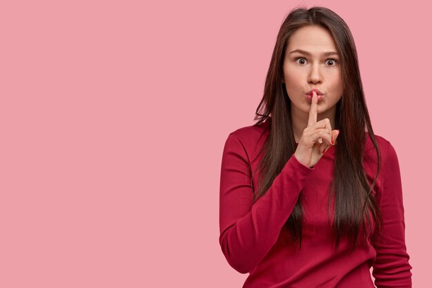 Jeune femme surprise fait un geste de silence, regarde avec une expression de panique, demande de ne pas dire secret, regarde inquiet