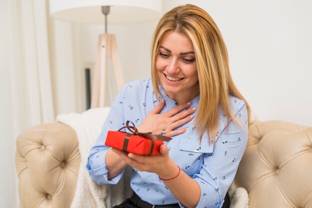 Jeune femme surprise heureuse avec boîte-cadeau sur le canapé