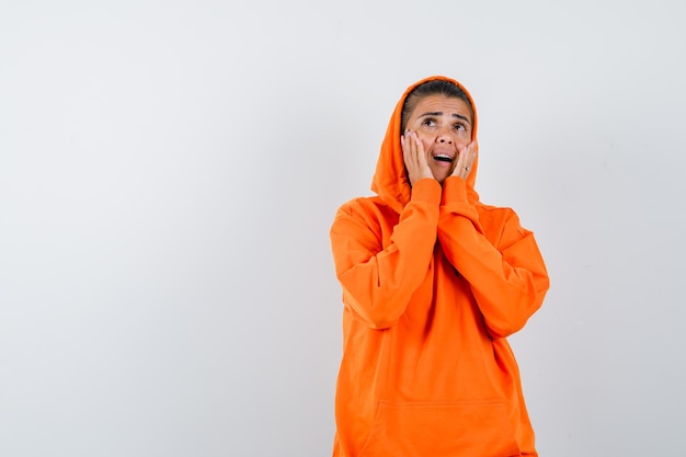 Jeune femme en sweat à capuche orange tenant la main près de la bouche comme appelant quelqu'un et ayant l'air concentré