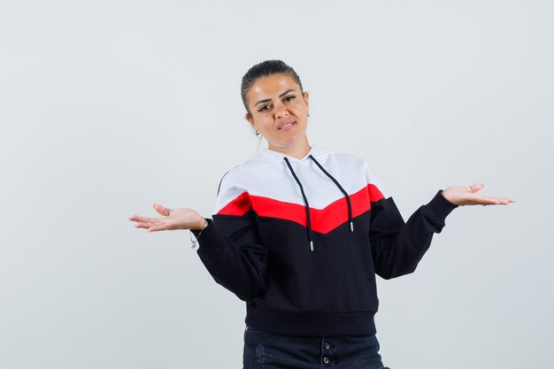 Jeune femme en sweat-shirt coloré montrant un geste impuissant et regardant sans espoir, vue de face.