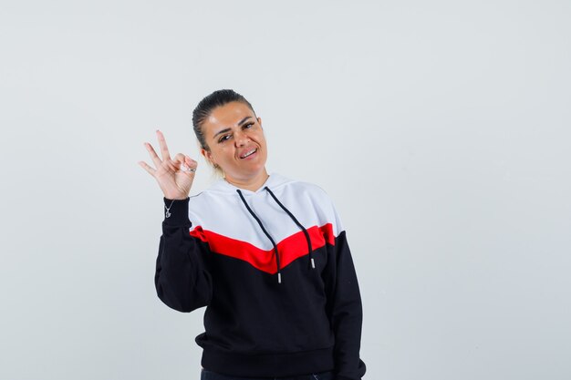 Jeune femme en sweat-shirt coloré montrant le geste ok et à la vue de face, heureux.