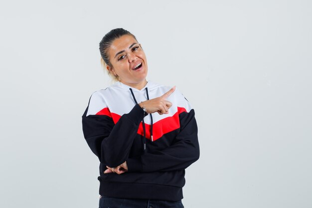 Jeune femme en sweat-shirt coloré pointant de côté et à la joyeuse vue de face.