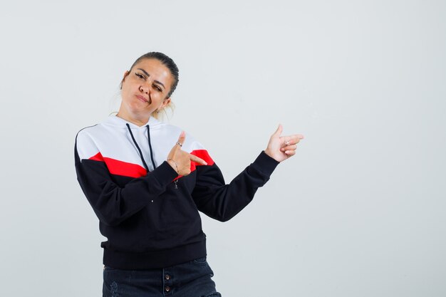 Jeune femme en sweat-shirt coloré pointant vers l'arrière et à la vue de face, confiant.