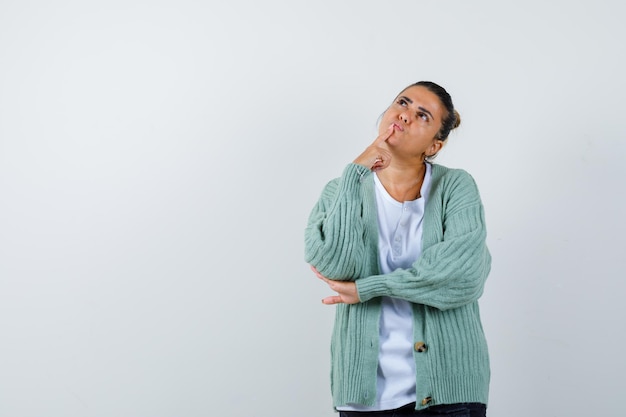 Jeune femme en t-shirt blanc et cardigan vert menthe debout dans une pose de réflexion et l'air pensif