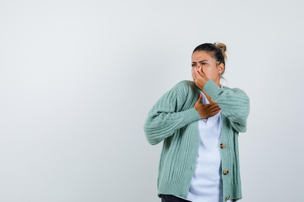 Jeune femme en t-shirt blanc et cardigan vert menthe pinçant le nez à cause d'une mauvaise odeur et ayant l'air ennuyé