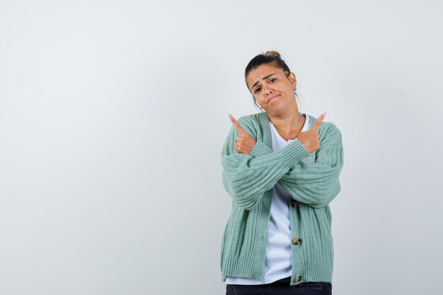 Jeune femme en t-shirt blanc et cardigan vert menthe pointant dans différentes directions avec l'index et à la triste