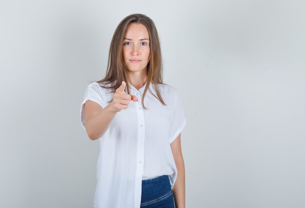 Photo gratuite jeune femme en t-shirt blanc, jeans pointant le doigt vers la caméra et à la joie