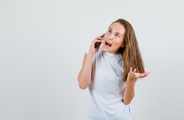 Jeune femme en t-shirt blanc parlant sur smartphone et à la drôle