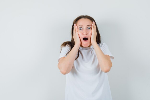 Jeune femme en t-shirt blanc tenant des paumes sur les joues et à la béatitude