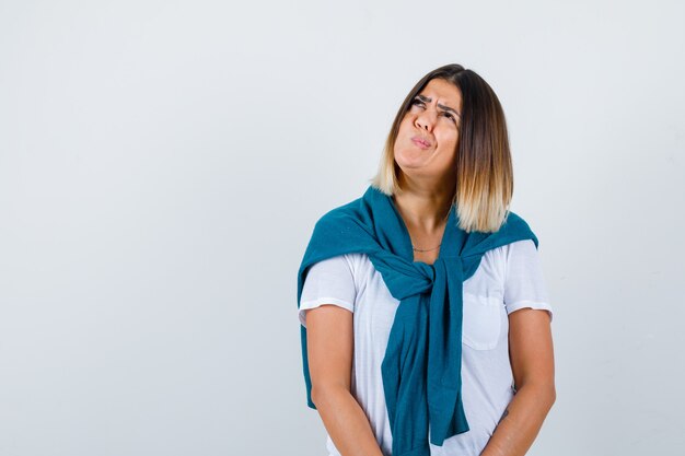 Jeune femme en t-shirt blanc tordant la bouche sur le côté et à la nostalgie, vue de face.