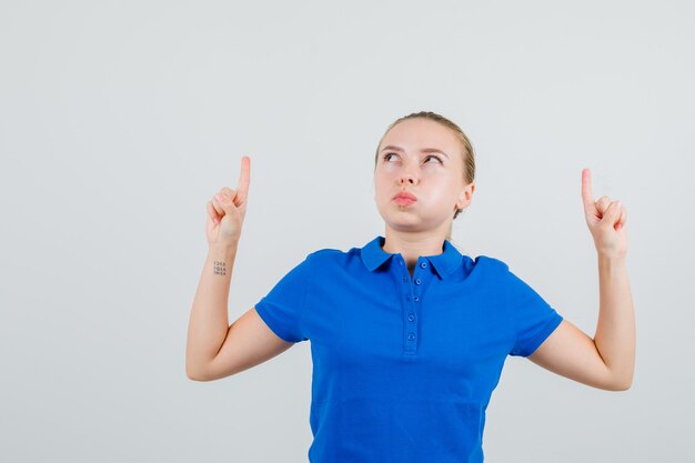 Jeune femme en t-shirt bleu pointant vers le haut et soufflant les joues