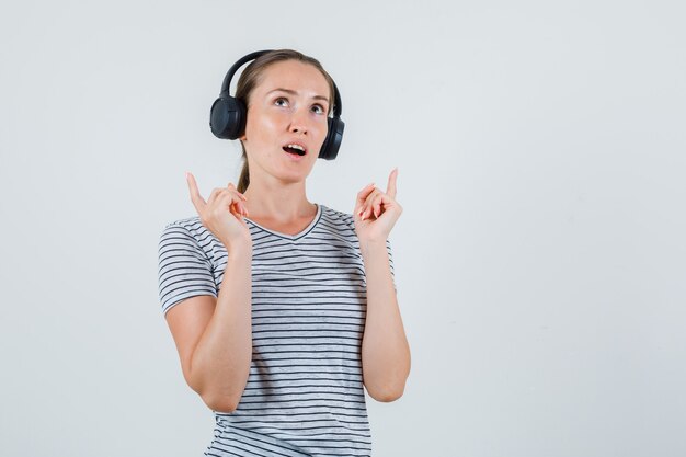 Jeune femme en t-shirt, casque pointant vers le haut et à l'espoir, vue de face.