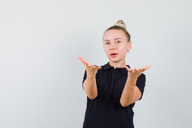 Jeune femme en t-shirt étirant les mains comme tenant ou montrant quelque chose et à la vue de face, confiant.