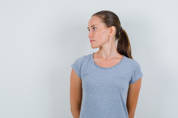 Jeune femme en t-shirt gris à côté et à la vue de face, focalisée.