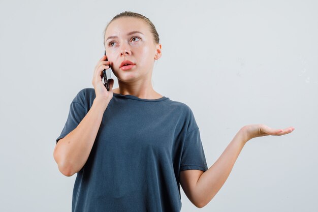 Jeune femme en t-shirt gris parlant au téléphone mobile et à la confusion