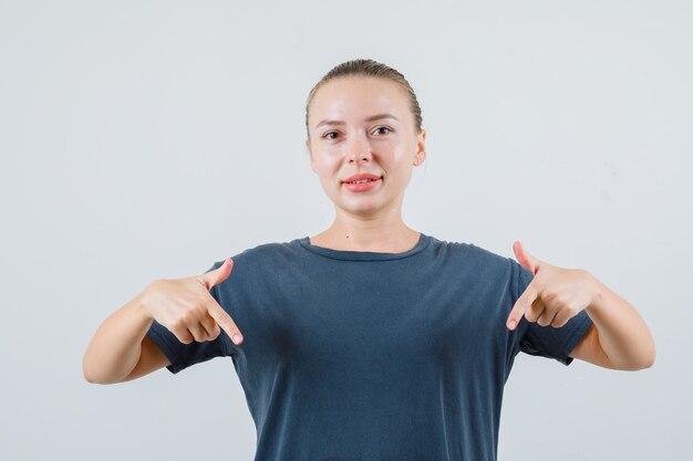 Jeune femme en t-shirt gris pointant vers le bas et souriant