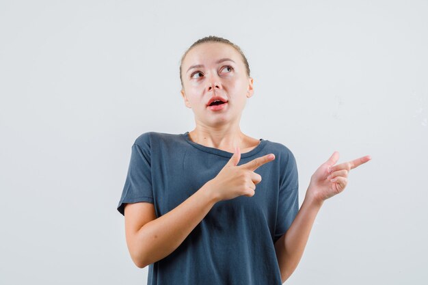 Jeune femme en t-shirt gris pointant vers le côté et à la curiosité