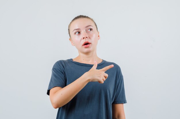 Jeune femme en t-shirt gris pointant vers le côté et à la curiosité