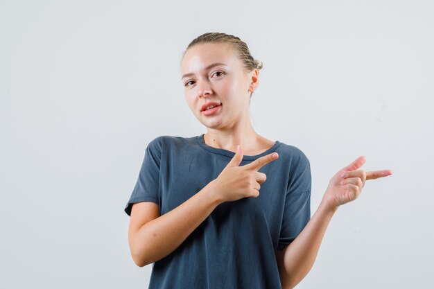 Jeune femme en t-shirt gris pointant vers le côté avec le geste du pistolet et à la joyeuse