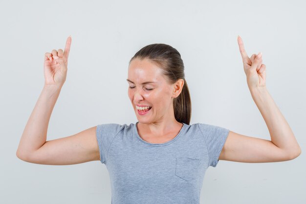 Jeune femme en t-shirt gris pointant vers le haut et à la vue de face, confiant.