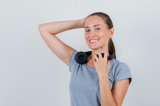 Jeune femme en t-shirt gris tenant les mains sur la tête et les écouteurs, vue de face.