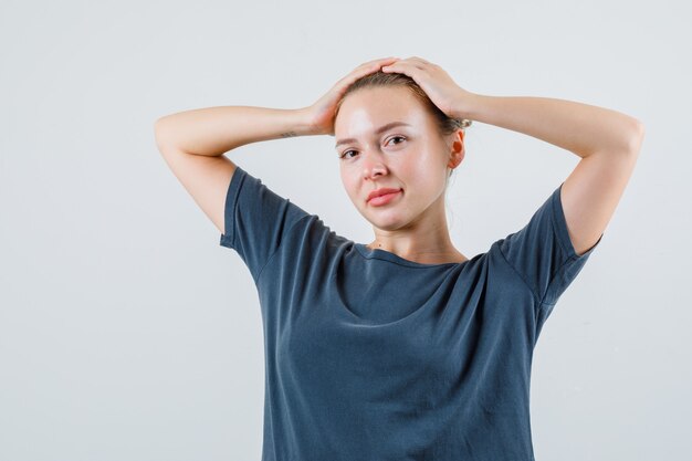 Jeune femme en t-shirt gris tenant les mains sur la tête et souriant