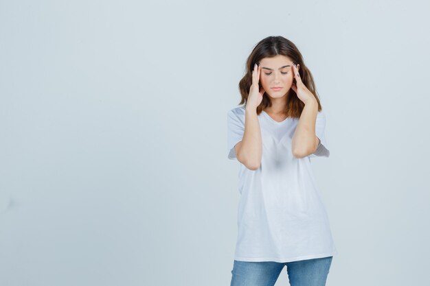 Jeune femme en t-shirt, jeans frottant ses tempes et à la fatigue, vue de face.