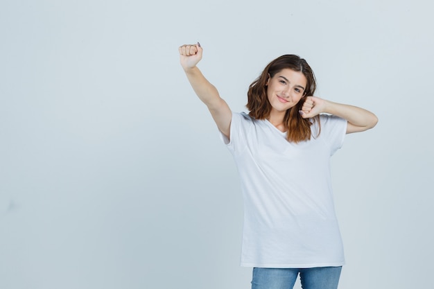 Jeune femme en t-shirt, jeans montrant le geste du gagnant et l'air heureux, vue de face.