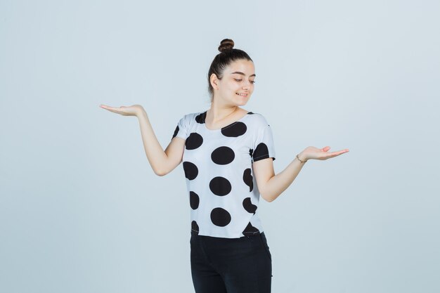 Jeune femme en t-shirt, jeans montrant le geste des échelles et l'air heureux, vue de face.