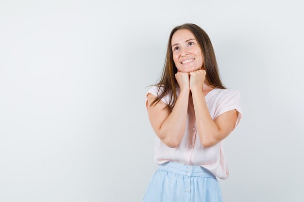 Jeune femme en t-shirt, jupe étayant le menton sur les poings et à l'espoir, vue de face.