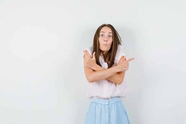 Jeune femme en t-shirt, jupe haussant les épaules tout en pointant vers l'extérieur et à la vue confuse, de face.