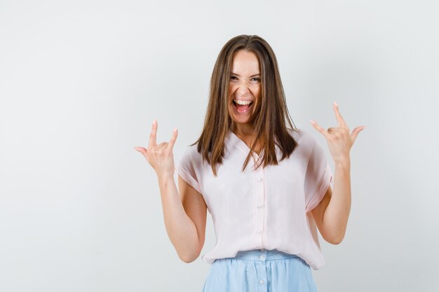 Jeune femme en t-shirt, jupe montrant le geste `` je t'aime '' et l'air fou, vue de face.