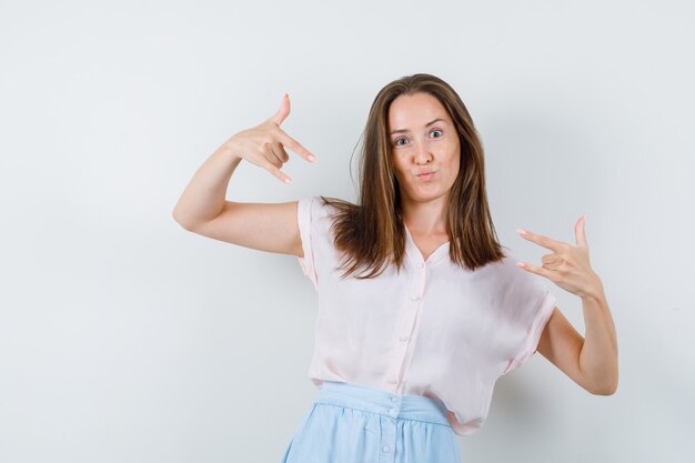 Jeune femme en t-shirt, jupe montrant le geste «je t'aime», vue de face.