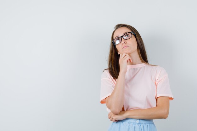 Jeune femme en t-shirt, jupe regardant vers le haut et regardant pensif, vue de face.