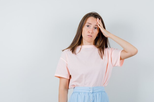 Jeune femme en t-shirt, jupe touchant son front et à la perplexité, vue de face.