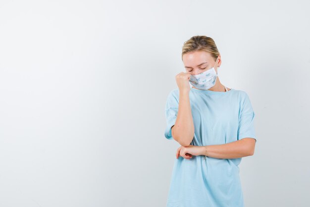 Jeune femme en t-shirt, masque gardant la main près du visage et ayant l'air fatigué