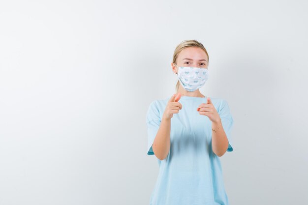 Jeune femme en t-shirt, masque pointant vers la joie